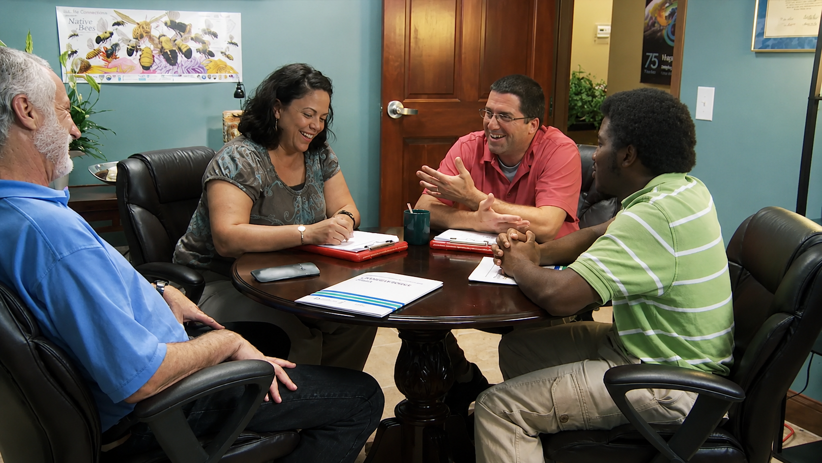 Four employees casually talking and laughing around a table in a conference room.